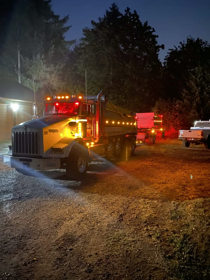 A Kenworth dump truck lit up with amber and red marker lights on a gravel drive at night.